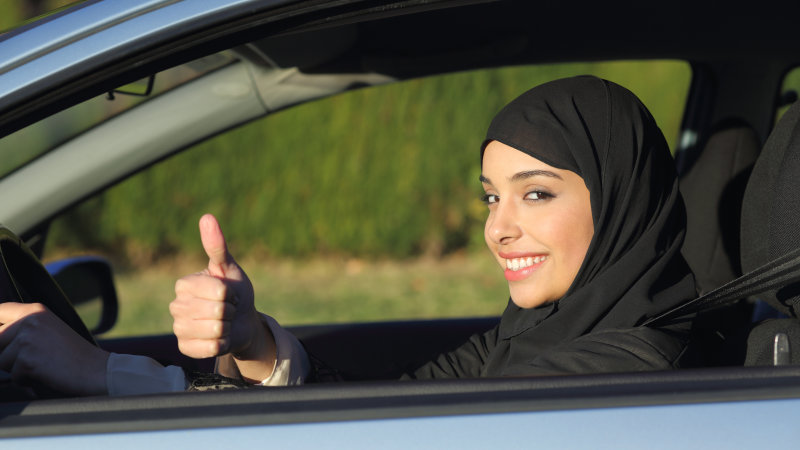 Happy arab saudi woman driving a car with thumb up smiling with a headscarf